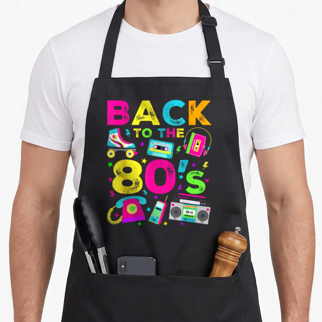 Funny eighty 80s apron - Stacked BACK TO THE 80'S text with roller skate, boombox, cassette, rotary phone in pink — shown on a black cotton canvas apron against a white background