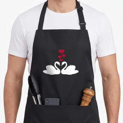 Funny i love my swan apron - Two white swans face each other with necks forming a heart, four red hearts float above — shown on a black cotton canvas apron against a white background
