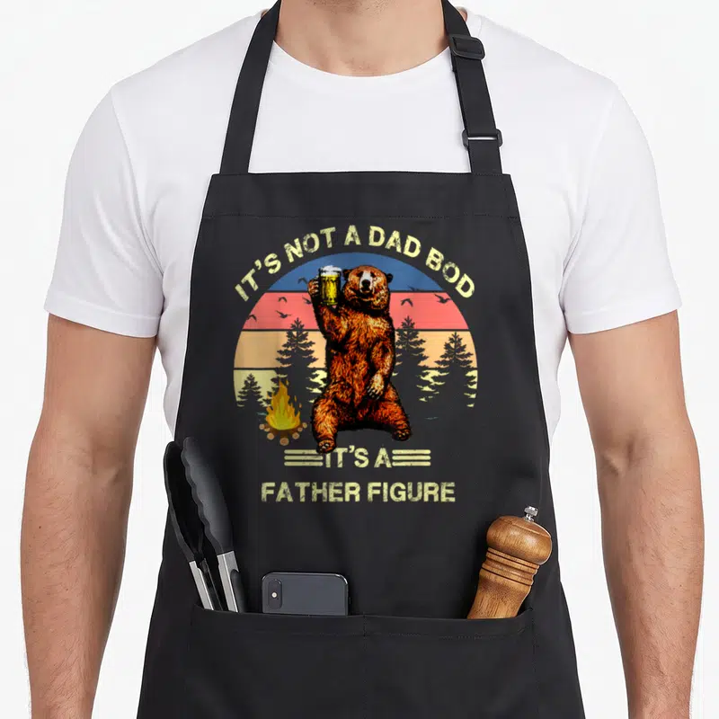 Funny father dad bod apron - Retro bear holding beer mug with IT'S NOT A DAD BOD text — shown on a black cotton canvas apron against a white background