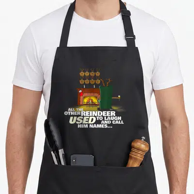 Nosed reindeer apron - Cartoon reindeer in green chair facing fireplace with eight heads on wall and stacked white text — shown on a black cotton canvas apron against a white background
