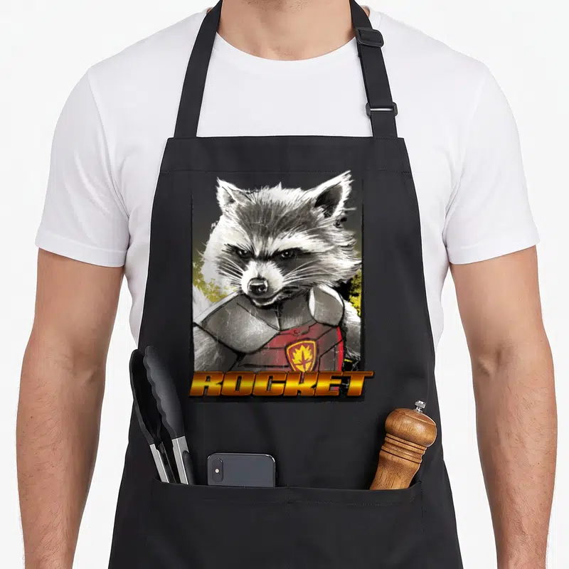 Glare arugula apron - Realistic Rocket Raccoon portrait with ROCKET text in grey black yellow and red — shown on a black cotton canvas apron against a white background