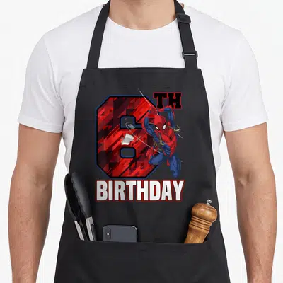 Swing 6th birthday apron - Leaping superhero in red and blue in front of number 6 with TH BIRTHDAY text — shown on a black cotton canvas apron against a white background