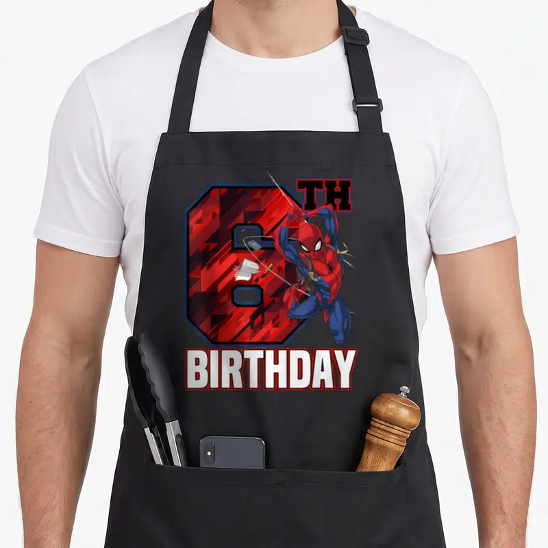 Swing 6th birthday apron - Leaping superhero in red and blue in front of number 6 with TH BIRTHDAY text — shown on a black cotton canvas apron against a white background
