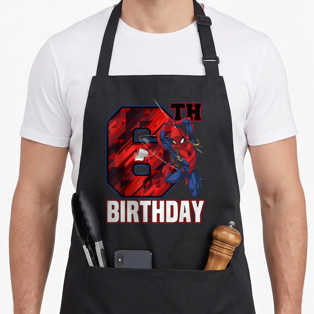 Swing 6th birthday apron - Leaping superhero in red and blue in front of number 6 with TH BIRTHDAY text — shown on a black cotton canvas apron against a white background