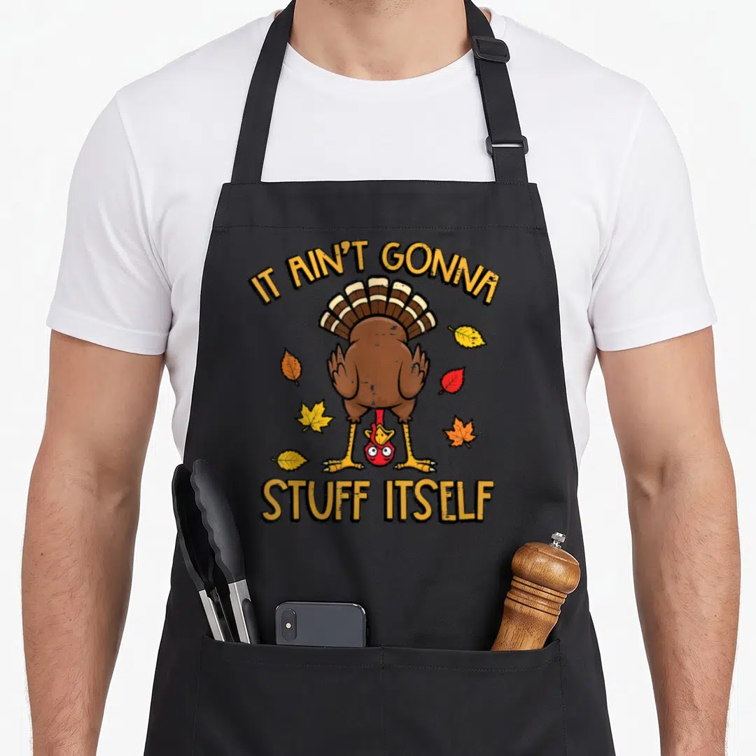Itself thanksgiving apron - Cartoon turkey standing on head with text IT AIN'T GONNA STUFF ITSELF and autumn leaves — shown on a black cotton canvas apron against a white background