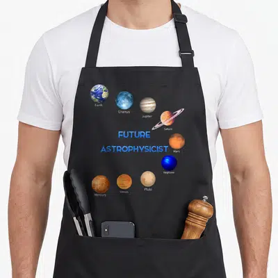 Future astronomy lover apron - Nine labeled planets orbiting FUTURE ASTROPHYSICIST text in blue orange brown white — shown on a black cotton canvas apron against a white background