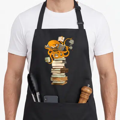 Reading coffee apron - Orange octopus perched on stacked books holding open pages and checkered tea set — shown on a black cotton canvas apron against a white background