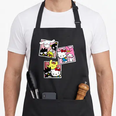 Booth friends apron - Three polaroid frames with cartoon characters in white, red, pink, yellow, and black — shown on a black cotton canvas apron against a white background