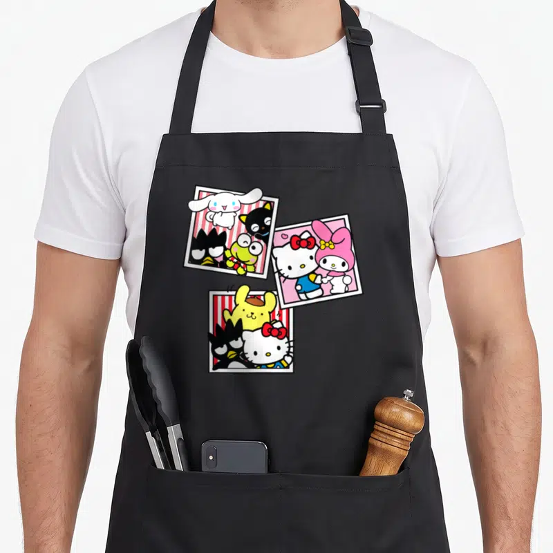 Booth friends apron - Three polaroid frames with cartoon characters in white, red, pink, yellow, and black — shown on a black cotton canvas apron against a white background
