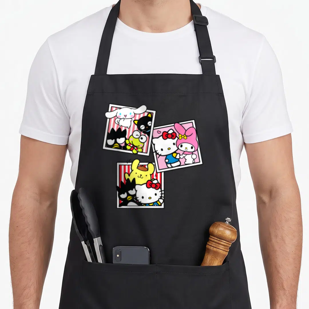 Booth friends apron - Three polaroid frames with cartoon characters in white, red, pink, yellow, and black — shown on a black cotton canvas apron against a white background