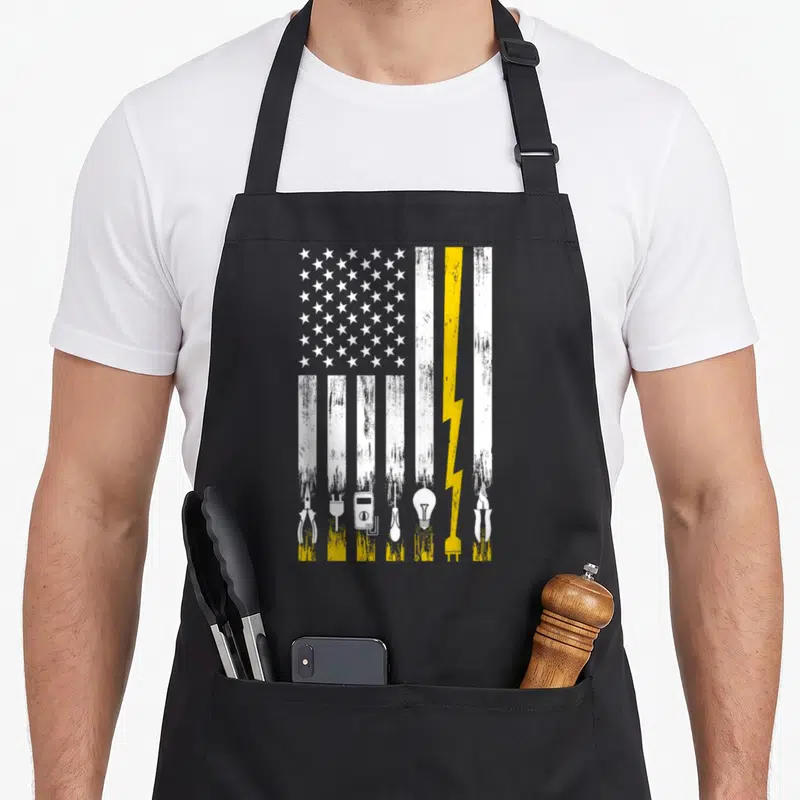 Engineer electrician apron - Distressed US flag with stripes made of pliers, multimeter, lightbulb, and yellow — shown on a black cotton canvas apron against a white background