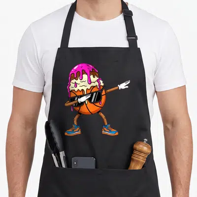 Dabbing ice cream apron - Cartoon orange basketball character with sunglasses and ice cream scoop doing a dab pose — shown on a black cotton canvas apron against a white background