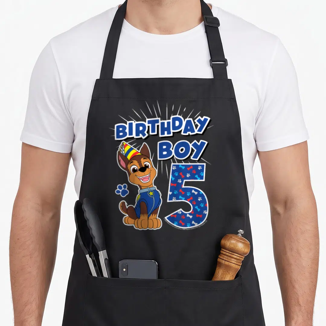 Chase age birthday apron - Cartoon dog with party hat next to number 5 filled with paw prints and bones — shown on a black cotton canvas apron against a white background