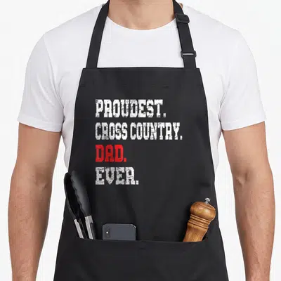 Cross track country apron - Stacked white and red text reading PROUDEST CROSS COUNTRY DAD EVER on black fabric — shown on a black cotton canvas apron against a white background