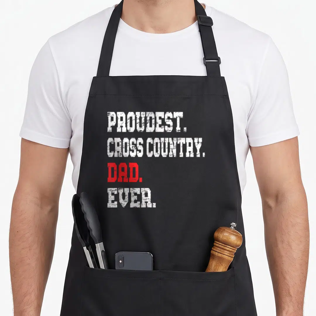 Cross track country apron - Stacked white and red text reading PROUDEST CROSS COUNTRY DAD EVER on black fabric — shown on a black cotton canvas apron against a white background