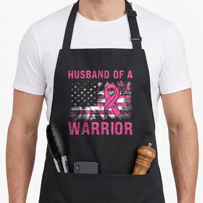 Warrior support breast cancer awareness aprons - Pink ribbon overlapping distressed flag with Husband of a Warrior text — shown on a black cotton canvas apron against a white background
