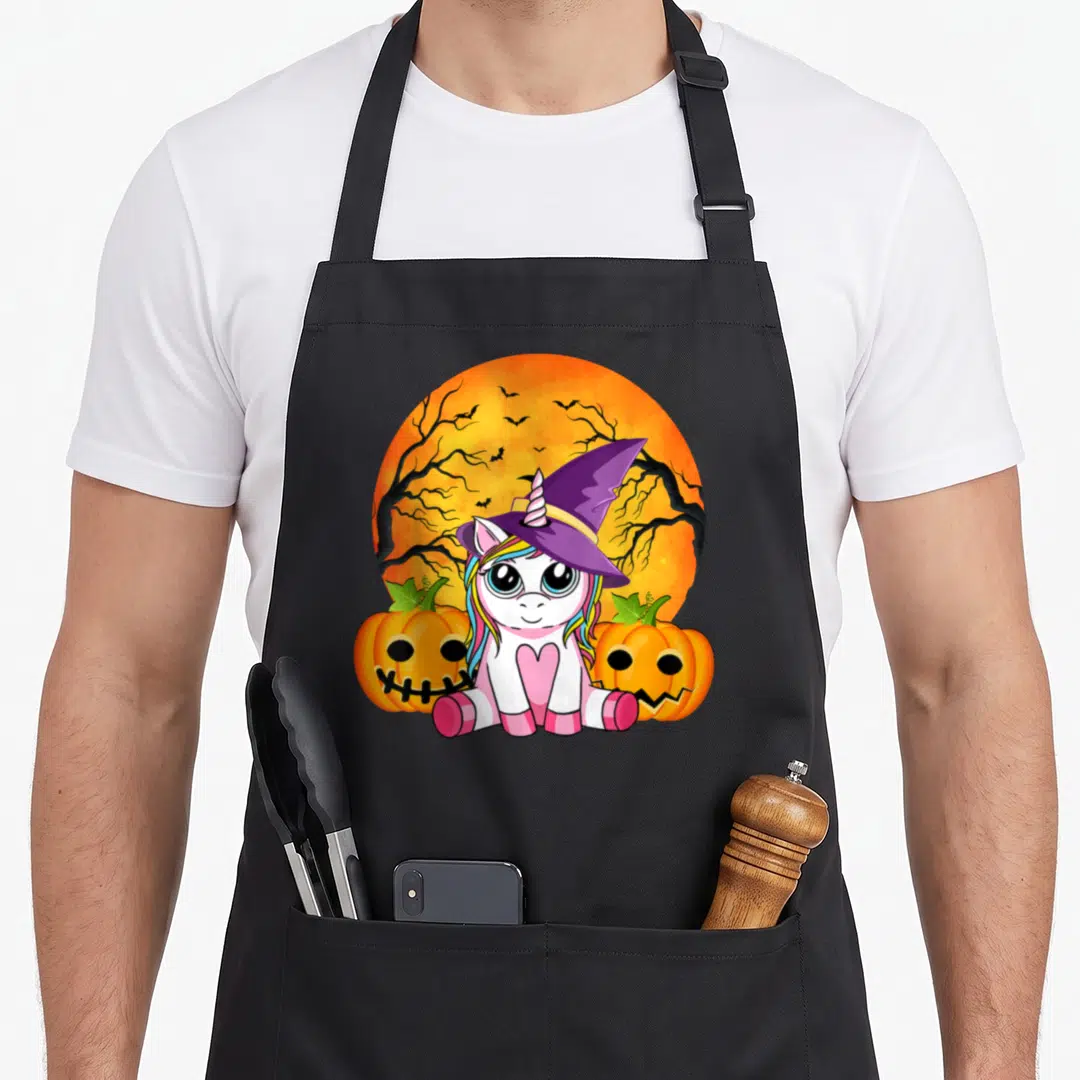Halloween unicorn apron - Cartoon unicorn in witch hat between two orange pumpkins under orange moon with bats — shown on a black cotton canvas apron against a white background