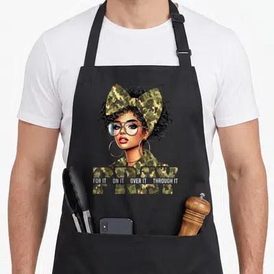 Afro christian apron - Camo PRAY text with cartoon woman in bow and glasses, white caption below — shown on a black cotton canvas apron against a white background