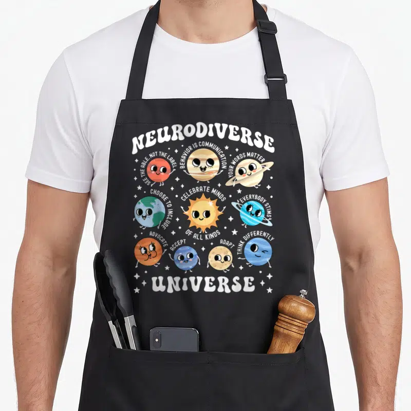 Neurodiverse special aprons - Cartoon planets with arched text Neurodiverse Universe and supportive messages — shown on a black cotton canvas apron against a white background
