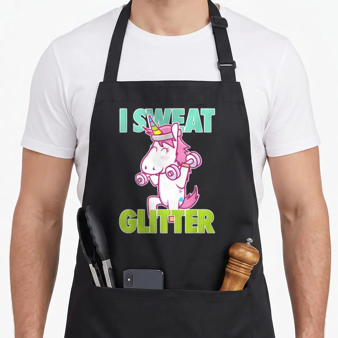 Sweat sassy apron - I Sweat Glitter text framing white unicorn lifting two dumbbells in mint and lime green — shown on a black cotton canvas apron against a white background