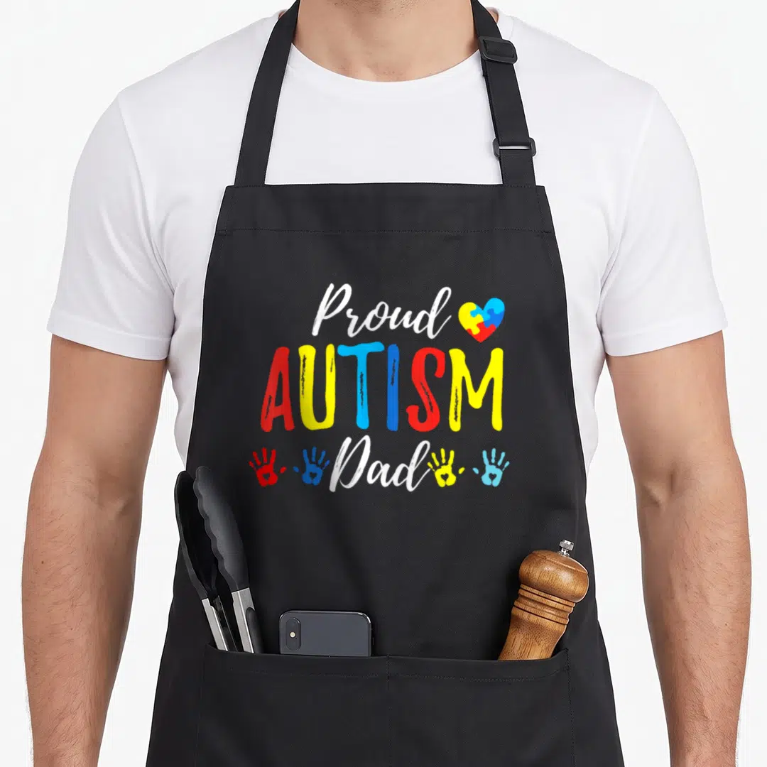 Autism family aprons - Proud AUTISM Dad text with puzzle heart and four colorful handprints in red yellow blue and white — shown on a black cotton canvas apron against a white background