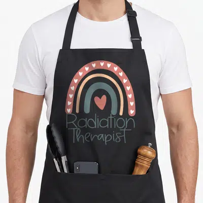 Graduation radiation aprons - Rainbow with white hearts and Radiation Therapist text in terracotta and blue-grey — shown on a black cotton canvas apron against a white background