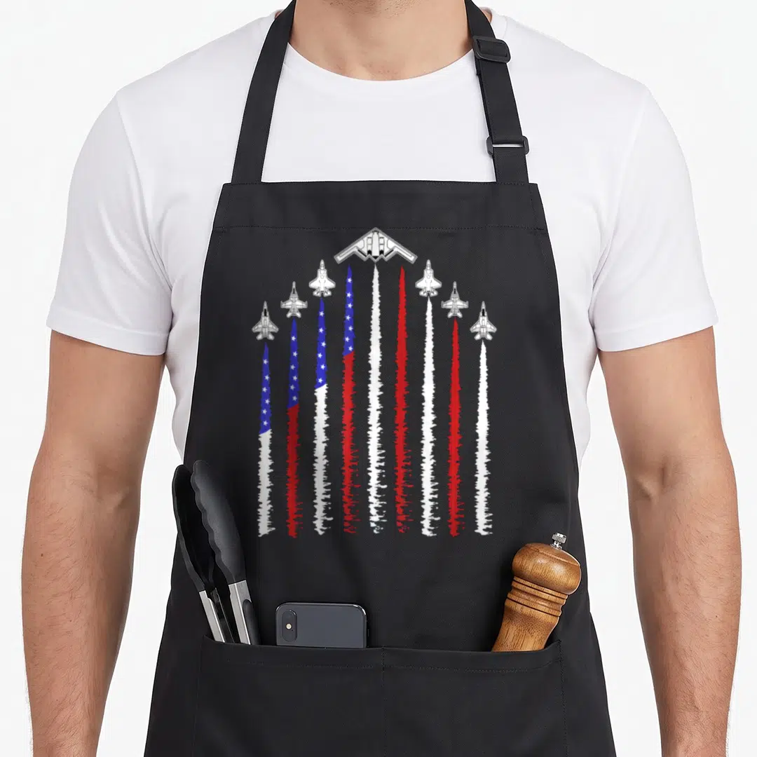 Jet patriotic 4th of july apron - Seven jets leaving red white and blue smoke trails forming a flag pattern — shown on a black cotton canvas apron against a white background