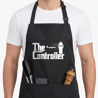 Controller aircraft apron - White 'The Controller' text, airplane with speed lines, and air traffic control tower — shown on a black cotton canvas apron against a white background