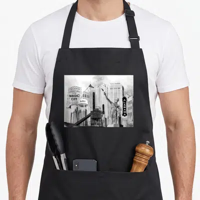 Landmark alabama apron - Black and white painting of Birmingham skyline with Sloss water tower, Magic City sign — shown on a black cotton canvas apron against a white background