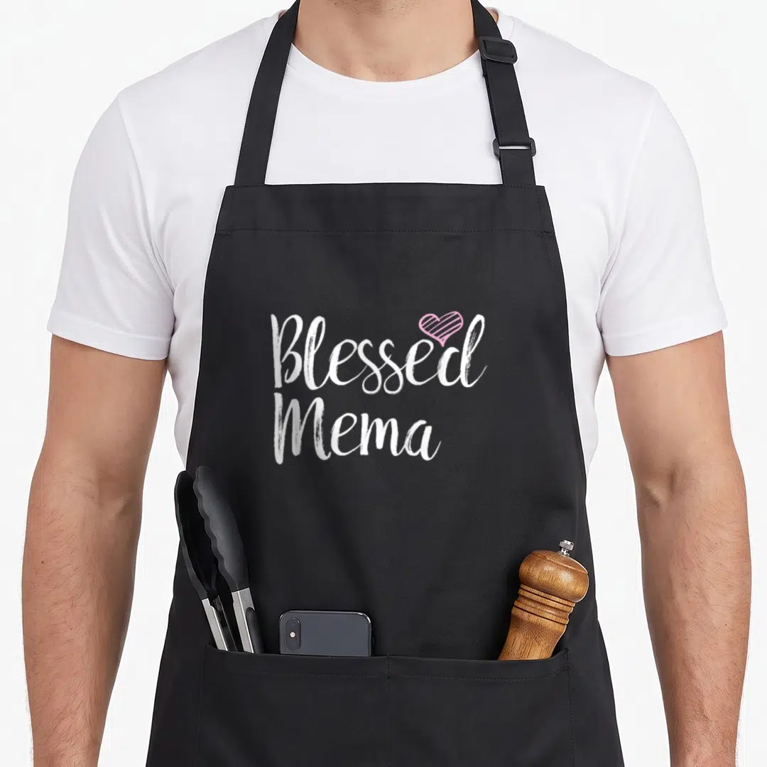 Blessed grandmother apron - Stacked white Blessed Mema text with pink striped heart overlapping top right — shown on a black cotton canvas apron against a white background