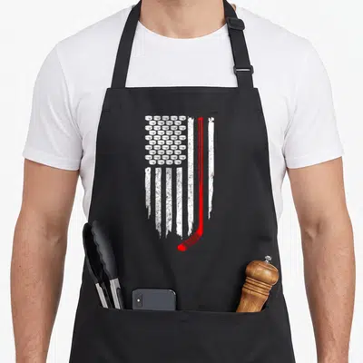 Hockey patriotic apron - Distressed USA flag with white hockey puck stars and red stick stripe on black background — shown on a black cotton canvas apron against a white background