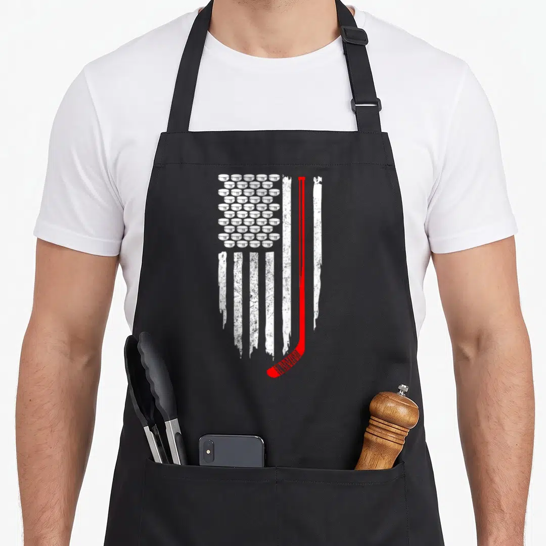 Hockey patriotic apron - Distressed USA flag with white hockey puck stars and red stick stripe on black background — shown on a black cotton canvas apron against a white background
