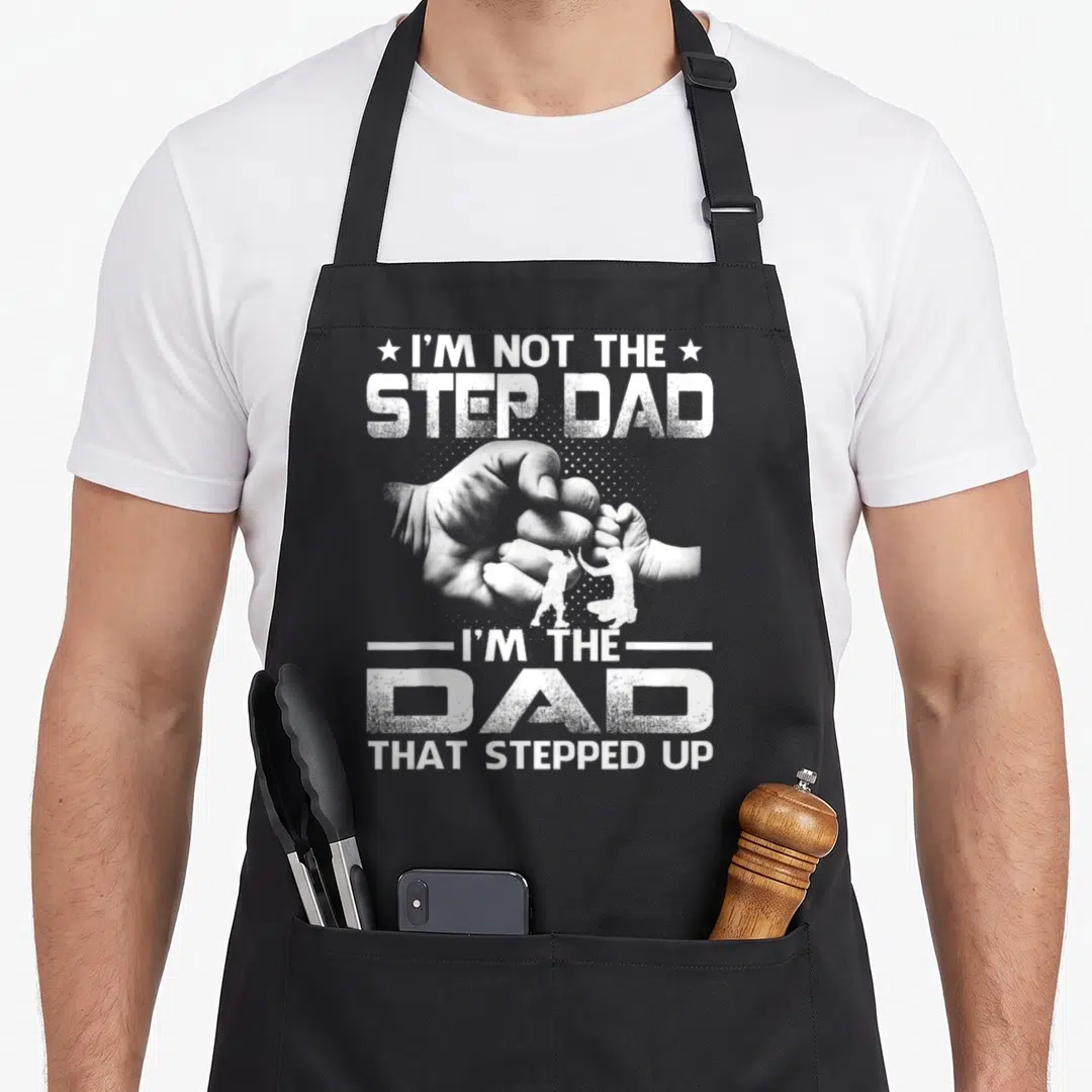 Stepped stepdad apron - White distressed text I'm Not The Step Dad surrounding a fist bump and small silhouettes — shown on a black cotton canvas apron against a white background