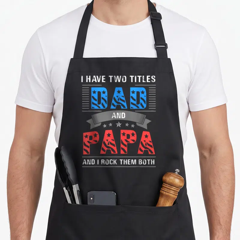 Funny papa father day apron - Stacked text I HAVE TWO TITLES DAD AND PAPA AND I ROCK THEM BOTH in blue red and grey — shown on a black cotton canvas apron against a white background