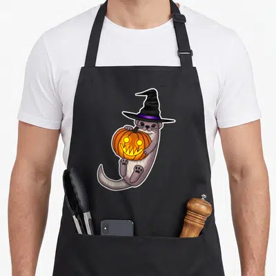 Otter halloween apron - Cartoon grey otter in black witch hat holding orange jack-o-lantern pumpkin — shown on a black cotton canvas apron against a white background