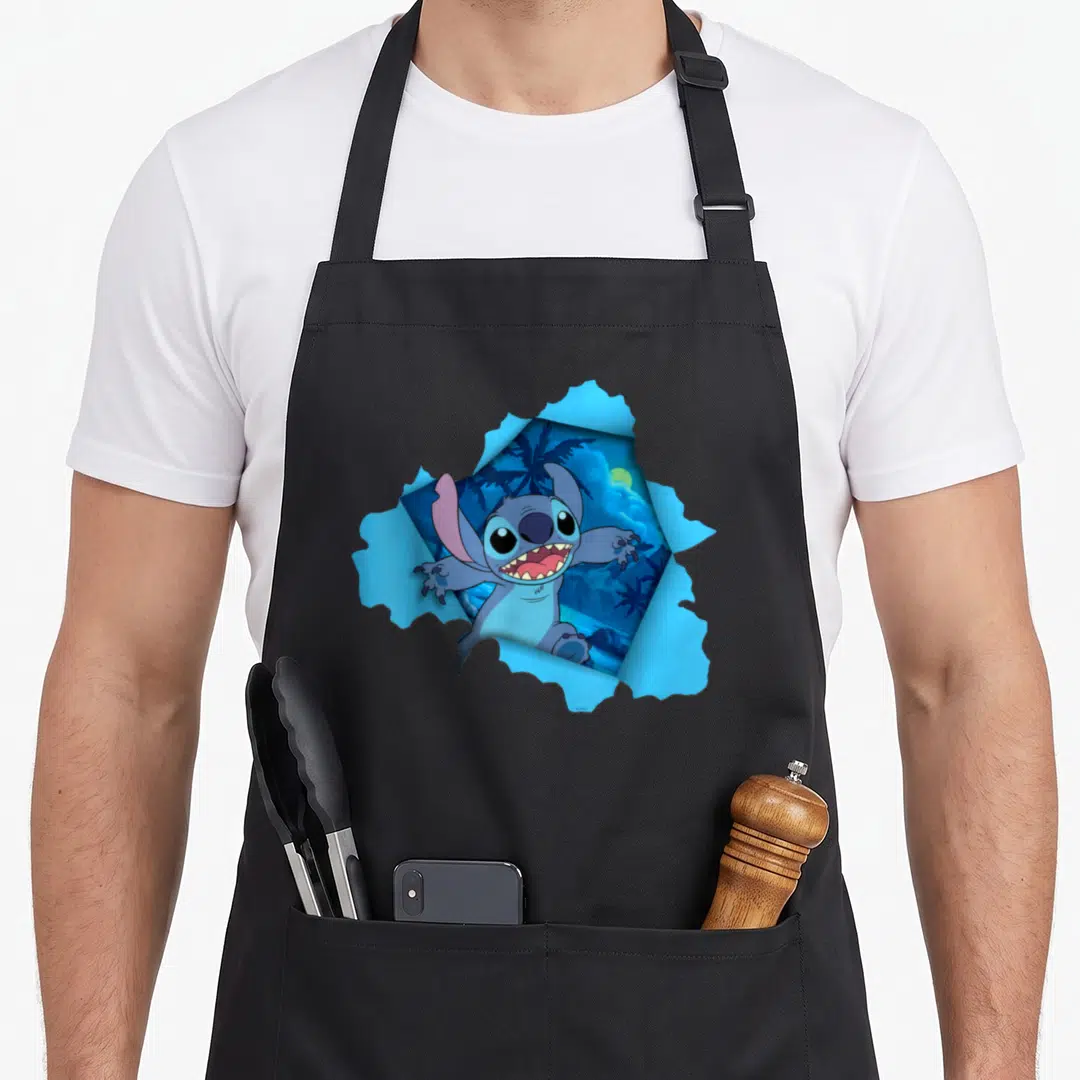 Tropical novelty apron - Stitch bursts through jagged light blue paper revealing a dark blue tropical night scene — shown on a black cotton canvas apron against a white background