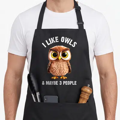 Zookeeper bird apron - Cartoon owl with I Like Owls & Maybe 3 People text in brown white and yellow — shown on a black cotton canvas apron against a white background