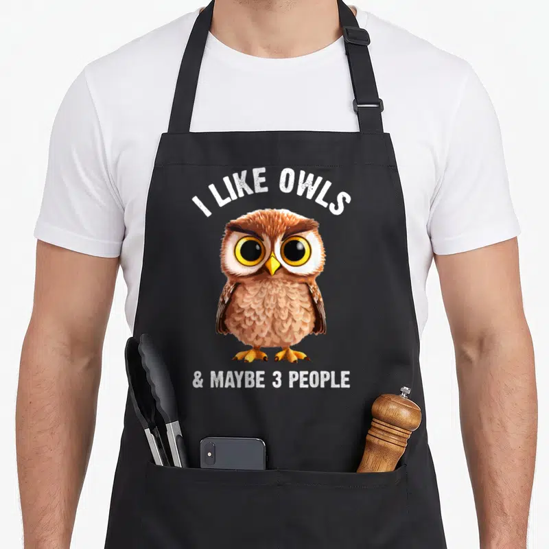 Zookeeper bird apron - Cartoon owl with I Like Owls & Maybe 3 People text in brown white and yellow — shown on a black cotton canvas apron against a white background