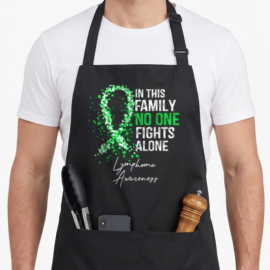 Lymphoma family aprons - Green and white ribbon made of small hearts next to text IN THIS FAMILY NO ONE FIGHTS ALONE — shown on a black cotton canvas apron against a white background