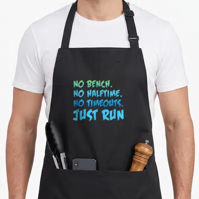 Running country apron - Stacked green and blue text reading NO BENCH NO HALFTIME NO TIMEOUTS JUST RUN — shown on a black cotton canvas apron against a white background