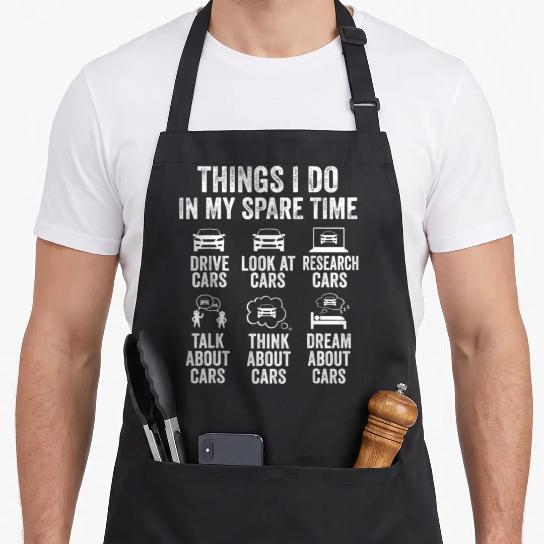 Spare garage apron - White distressed text listing six car activities with corresponding icons like driving and dreaming — shown on a black cotton canvas apron against a white background