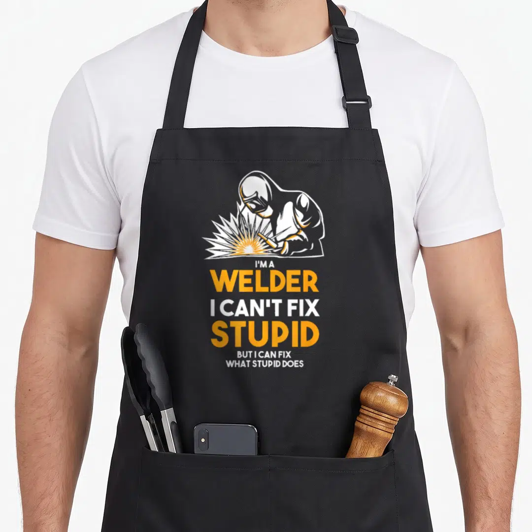 Welder stupid aprons - Cartoon welder with orange sparks and text reading I am a welder I cannot fix stupid — shown on a black cotton canvas apron against a white background