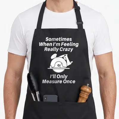 Funny carpenter woodworking apron - White circular saw graphic between lines of text reading Sometimes When I'm Feeling — shown on a black cotton canvas apron against a white background