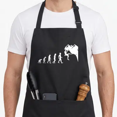 Rock climbing quotes apron - White evolution sequence silhouettes ending with a figure scaling a mountain peak — shown on a black cotton canvas apron against a white background