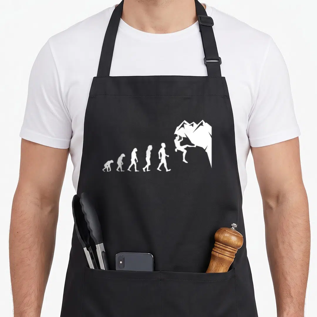 Rock climbing quotes apron - White evolution sequence silhouettes ending with a figure scaling a mountain peak — shown on a black cotton canvas apron against a white background