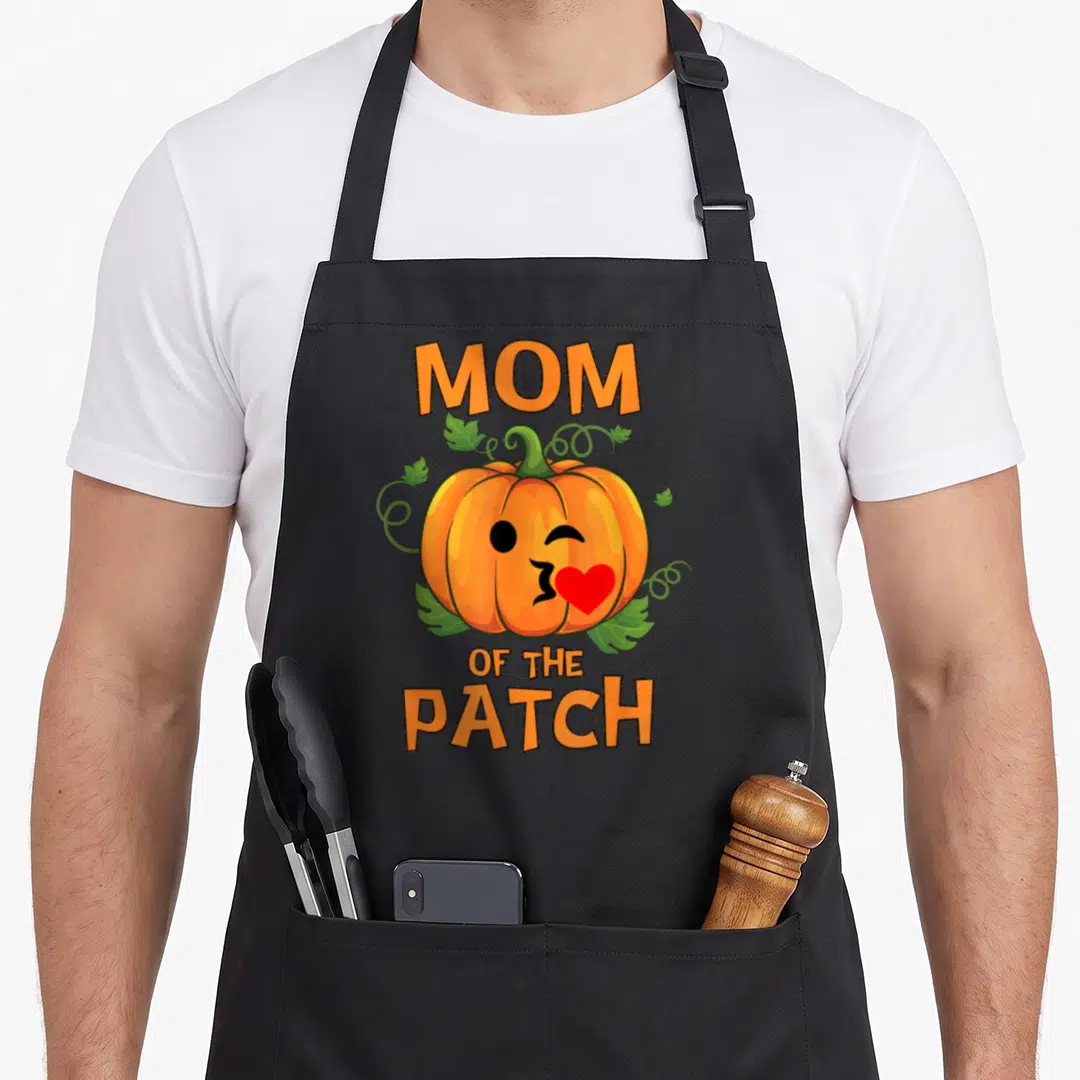 Patch family halloween apron - Orange pumpkin with red heart mouth and MOM OF THE PATCH text — shown on a black cotton canvas apron against a white background
