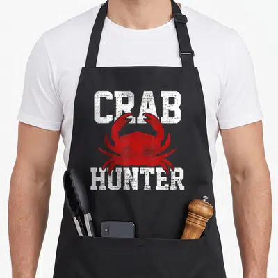 Funny crab apron - CRAB HUNTER text surrounding a red crab silhouette — shown on a black cotton canvas apron against a white background