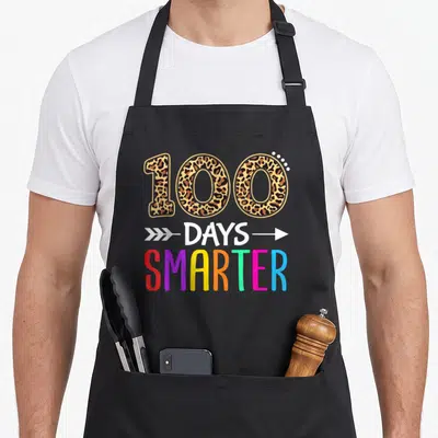 Smarter kindergarten boys apron - Leopard print 100 above white arrows and multicolored SMARTER text — shown on a black cotton canvas apron against a white background