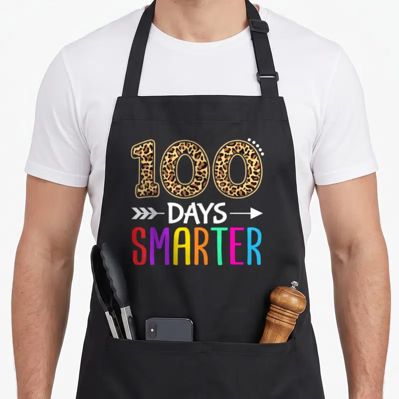 Smarter kindergarten boys apron - Leopard print 100 above white arrows and multicolored SMARTER text — shown on a black cotton canvas apron against a white background