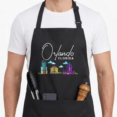 Orlando skyline florida apron - Cartoon Orlando Florida skyline with skyscraper, castle, clouds, and green trees — shown on a black cotton canvas apron against a white background